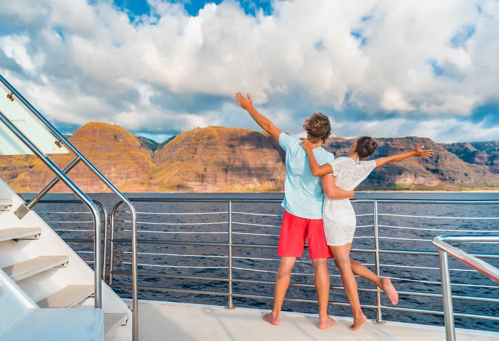 Couple on luxury yacht cruise ship tour at sunset feeling free happy with open arms in fun looking at mountain scenery.