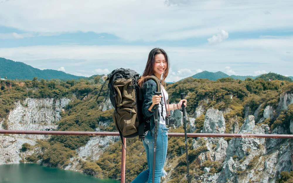 Asian beautiful woman wearing hat and casual clothes, smiling with happiness, adventure traveling alone and hiking on the top of mountains with backpack in summer vacation trip on weekend